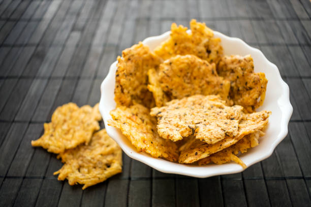 queso snack de patatas fritas en un tazón de fuente redondo blanco sobre un fondo negro de madera. chips de queso cheddar crujientes dippable libre grano, keto y baja en carbohidratos. chip crujiente bocado de queso cheddar, parmesano, asiago, hierbas, es - cheese and crackers fotografías e imágenes de stock