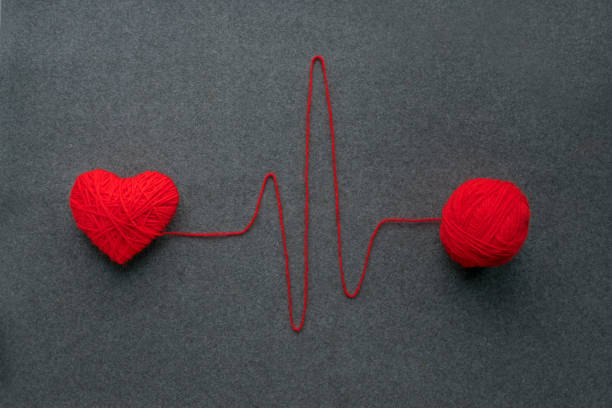 istock Handmade red yarn ball with heart made of red wool yarn and thread like ECG pattern on a gray woolen fabric background. Red warm heart like a symbol of love. Heart health, heartbeat, feelings, love, romance concept 1017030448