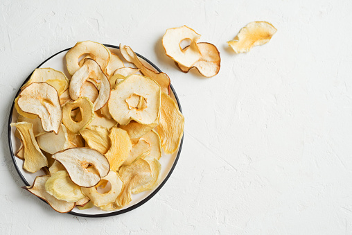 Various fruit chips on white background, copy space. Assorted dehydrated apple, pear, melon, mango fruit chips - healthy vegan snack.