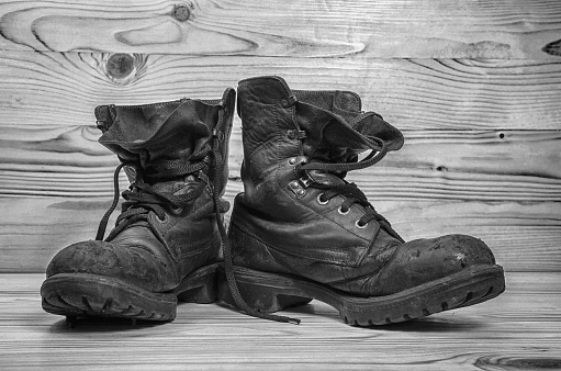 Old military boots on a wooden table in black and white.