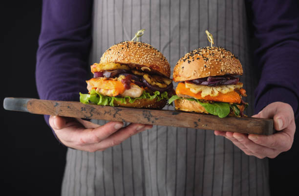 istock Chicken burger with pineapple. Men's hands hold a tray with a cheeseburger 1017068524