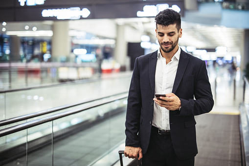 Businessman at airport with smartphone and suitcase