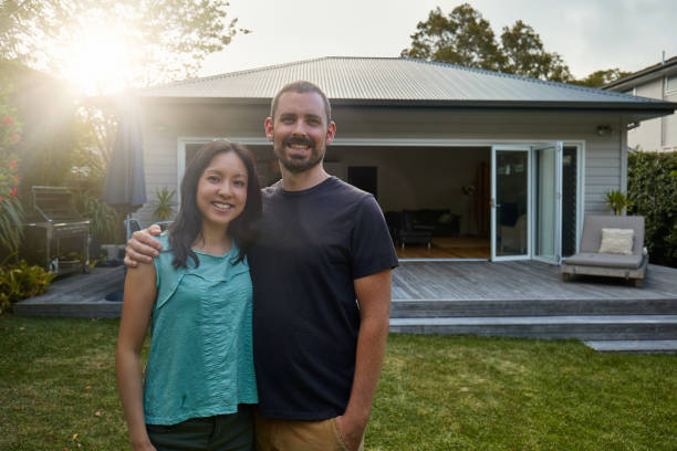 Smiling mid adult couple standing against house Portrait of smiling mid adult couple standing against house during sunset. Happy man and woman are in lawn at back yard. They are in casuals. 30 39 years photos stock pictures, royalty-free photos & images