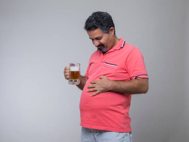 prise de vue studio d’un homme en surpoids avec un verre de bière - pot belly greed overweight excess photos et images de collection