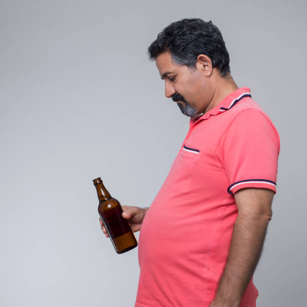 prise de vue studio d’un homme en surpoids avec un verre de bière - pot belly greed overweight excess photos et images de collection