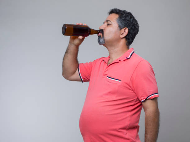 prise de vue studio d’un homme en surpoids avec un verre de bière - pot belly greed overweight excess photos et images de collection