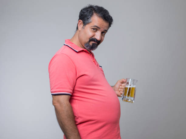 prise de vue studio d’un homme en surpoids avec un verre de bière - pot belly greed overweight excess photos et images de collection