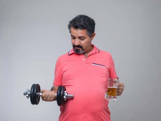 prise de vue studio d’un homme en surpoids avec un verre de bière - pot belly greed overweight excess photos et images de collection