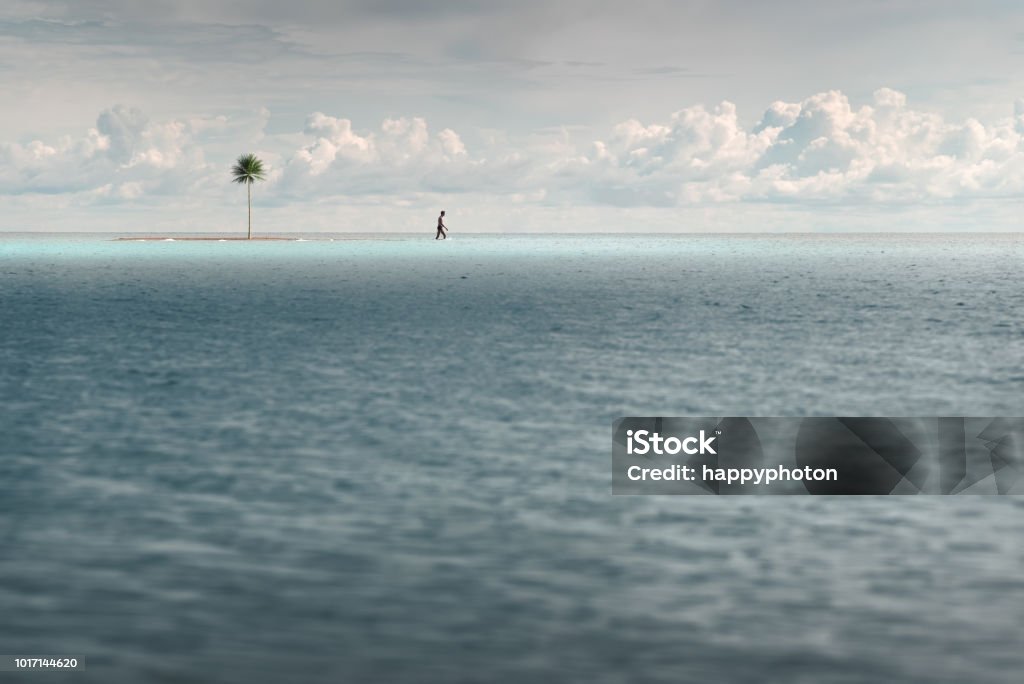 A man walks in shallow turquoise water. Near a small uninhabited island A man walks in shallow turquoise water. Near a small uninhabited island with a palm tree Abandoned Stock Photo