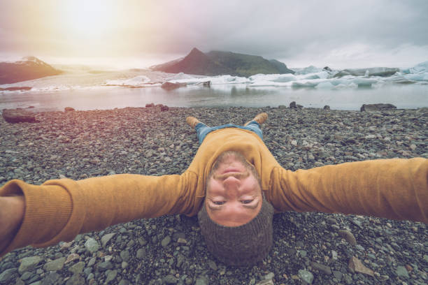istock Young man taking upside down selfie with glacier lake, icebergs floating on water 1017147562