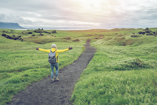 Caucasian female hiking arms raised for positive emotions, nature background with grass and mountains. Shot in West Iceland, Springtime. People travel hiking lifestyles concept