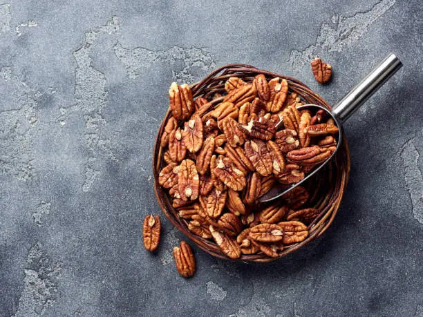 Pecan nuts and scoop on gray concrete background