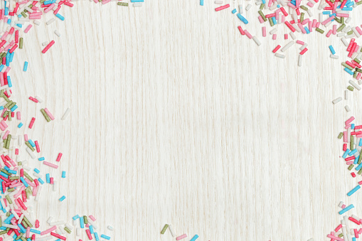 Colorful sprinkles around wooden background, party design element. Festive holiday frame with copy space. Celebration concept.