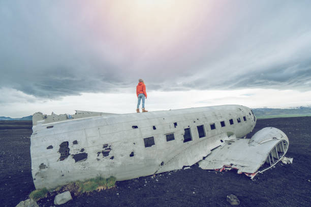 istock Young woman stands on airplane crashed on black sand beach looking around her contemplating surroundings 1017187436
