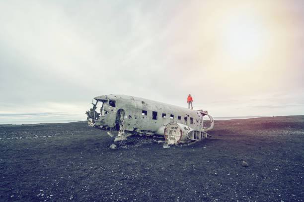 istock Young woman stands on airplane crashed on black sand beach looking around her contemplating surroundings 1017187456