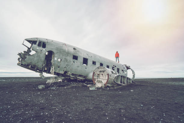 istock Young woman stands on airplane crashed on black sand beach looking around her contemplating surroundings 1017189608
