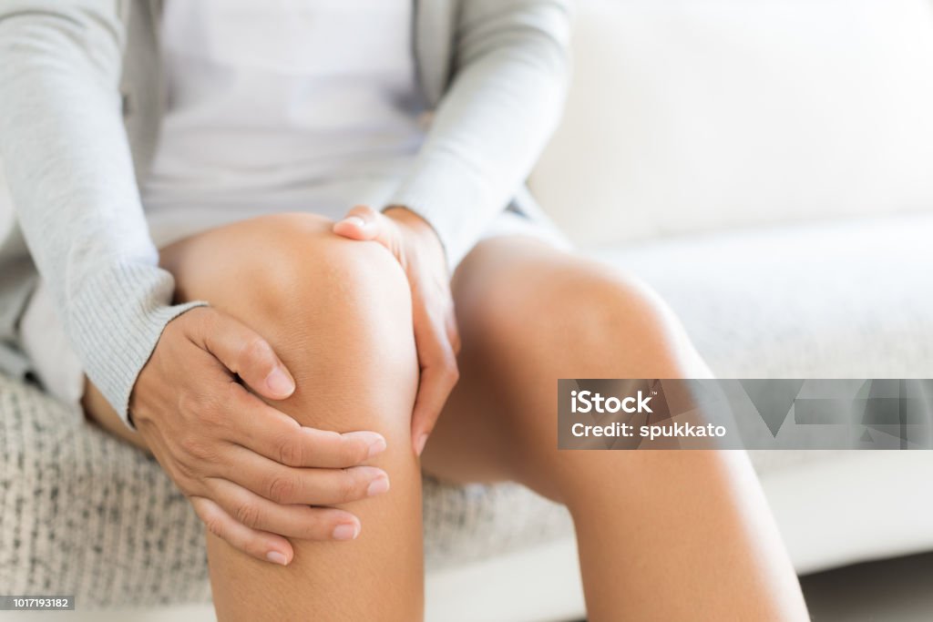 Closeup jeune femme assise sur le canapé et le sentiment genou douleur et elle massage son genou à la maison. Concept de soins de santé et médical. - Photo de Genou libre de droits