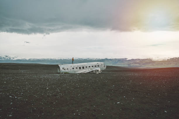 istock Young man stands on airplane crashed on black sand beach looking around her contemplating surroundings 1017193382