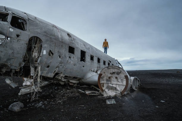 istock Young man stands on airplane crashed on black sand beach looking around her contemplating surroundings 1017193608