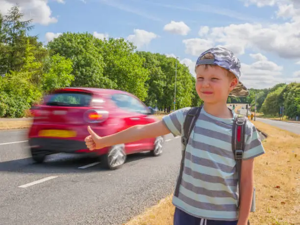 Photo of Day view little child boy traveler with backpack catching car on UK road