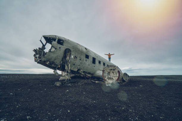 istock Young man stands arms outstretched on airplane crashed on black sand beach looking around her contemplating surroundings 1017196132