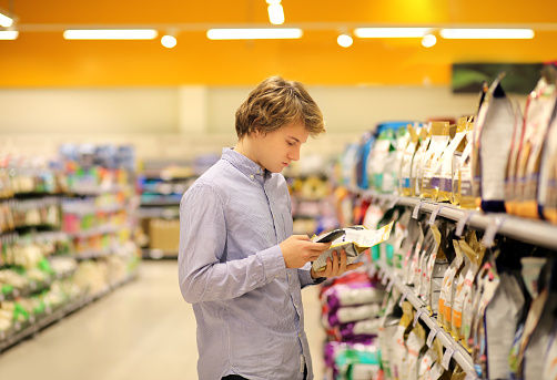 Hombre de compras en el supermercado leyendo información del producto. Utilizando smarthone. Alimentos para mascotas photo