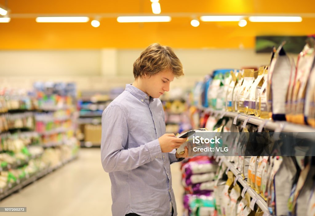 Man shopping in supermarket reading product information.Using smarthone.Pet food Supermarket Stock Photo