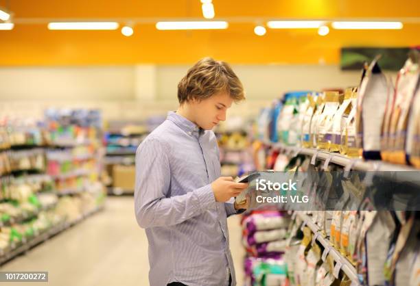 Man Shopping In Supermarket Reading Product Informationusing Smarthonepet Food Stock Photo - Download Image Now