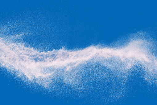 Abstract white dust explosion. Freeze motion of white particles on blue background