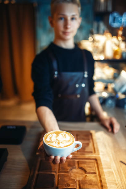 Male barista shows cup of coffee with foam drawing