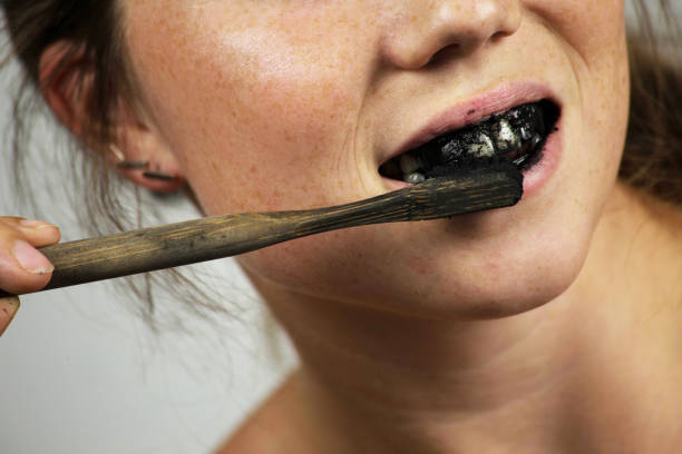 young woman brushing her teeth with a black tooth paste with active charcoal, and black tooth brush on white background for Teeth whitening stock photo