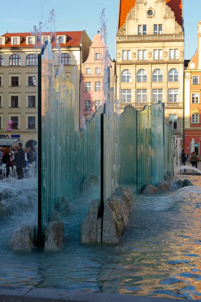 modern fountain in the shade at market square in wroclaw. the market square in wroclaw is one of the largest historical market squares in poland. there are many unidentified people who come to this old town square to spend their free time - editorial built structure fountain town square imagens e fotografias de stock