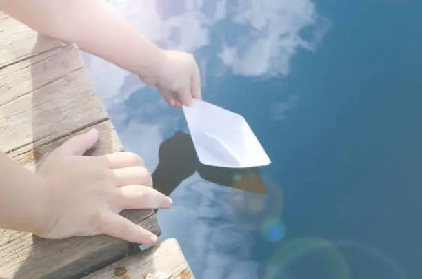 Hands of little boy, releases into the water paper boat with wooden pier.On sunny days.