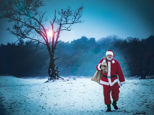 Santa Claus with a bag of gifts walking on snow-covered field.