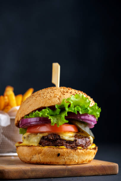 tasty grilled beef burger with lettuce, cheese and onion served on cutting board on a black wooden table, with copyspace. - take out food fast food vertical tomato imagens e fotografias de stock