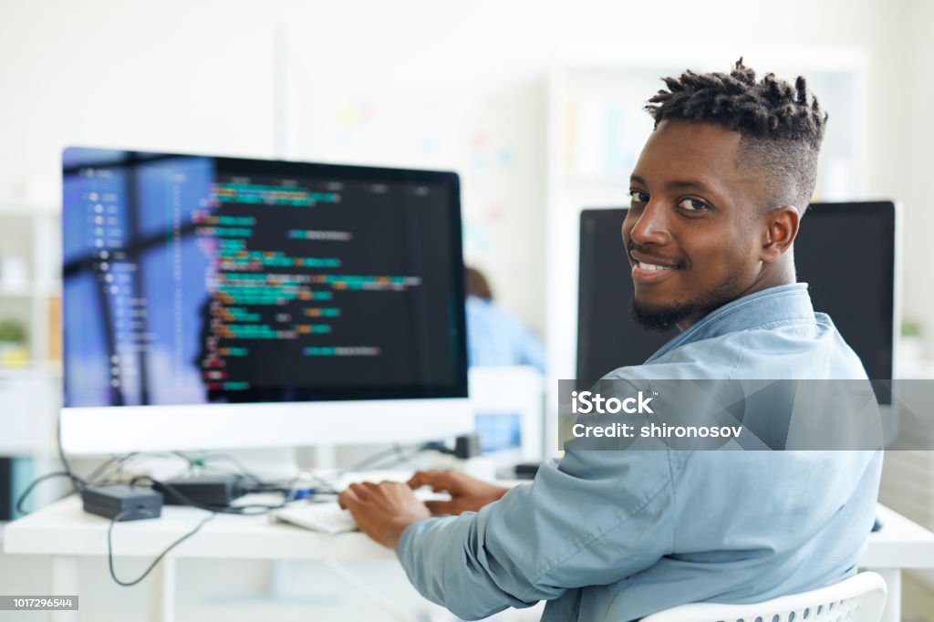 Testing software Happy guy looking at you while sitting by workplace and working with software Computer Programmer Stock Photo