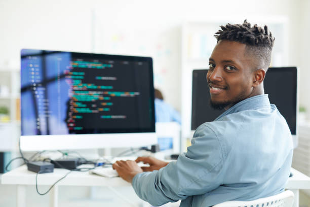 Testing software Happy guy looking at you while sitting by workplace and working with software programmer stock pictures, royalty-free photos & images