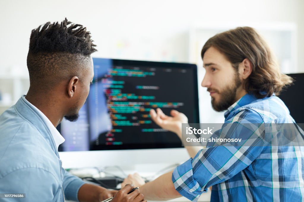 Meeting of programmers One of software developers pointing at computer screen while explaining his co-worker new method of data decoding Computer Programmer Stock Photo