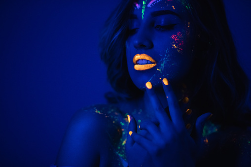 Young woman wearing fluorescent makeup in the dark