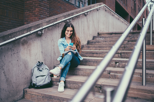 Young girl sitting on ground and using smartphone