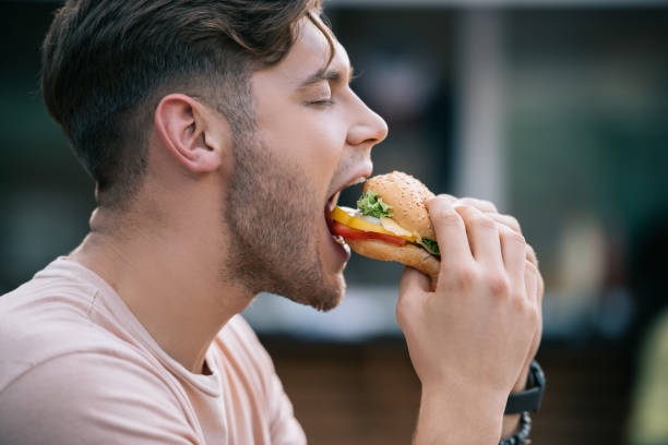 widok z boku człowieka jedzącego smacznego burgera z zamkniętymi oczami - sandwich burger take out food hamburger zdjęcia i obrazy z banku zdjęć