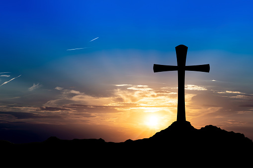 Silhouette of a big cross on a hill at sunset