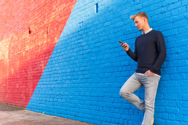Young man leaning against a brick wall while using a smart phone stock photo