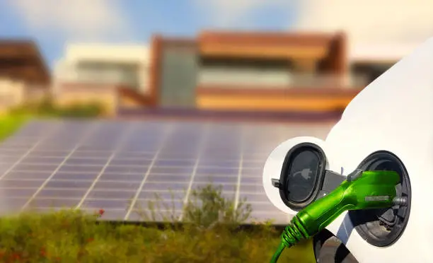 Close up view of Electric Car charging and houses with solar panels in the background