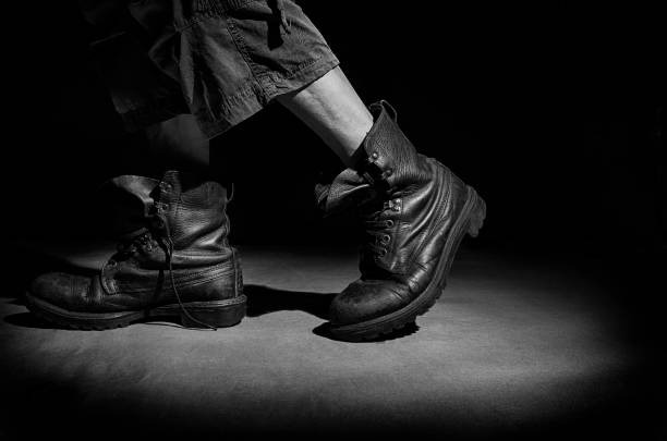 A man in old military boots leaves the circle of light, in black and white.