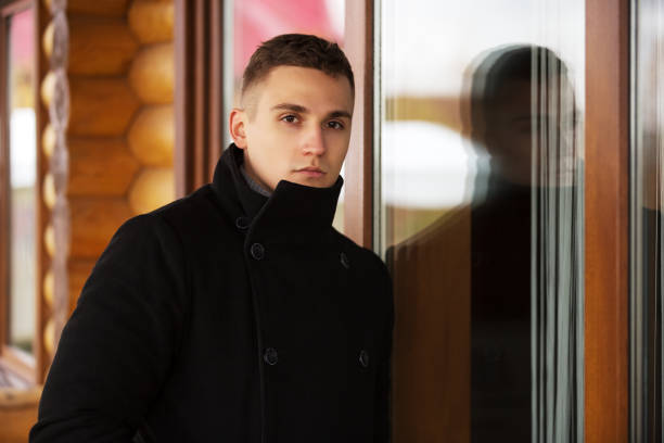 istock Young handsome man in classic black coat standing at the window 1017479574