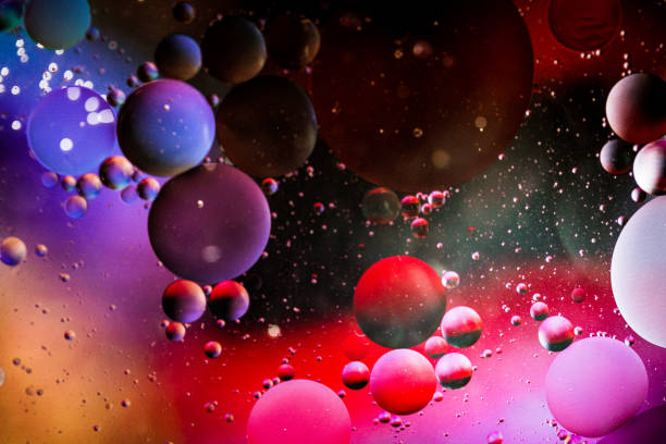 Close up macro image depicting droplets of oil in water on a multi colored background. The oil forms interesting circles and spheres in the water, and colorful background produces and abstract effect. Horizontal color image with copy space.