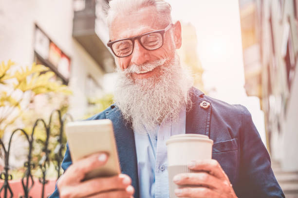 istock Happy senior man using smartphone app outdoor while drinking take away coffee - Fashion old guy having fun with new trend technology - Tech and joyful elderly lifestyle concept - Focus on his mouth 1017590874
