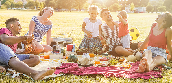 Happy families doing picnic in city park - Young parents having fun with their children in summer time eating, drinking and laughing together - Love and chlidood concept - Main focus on left man face