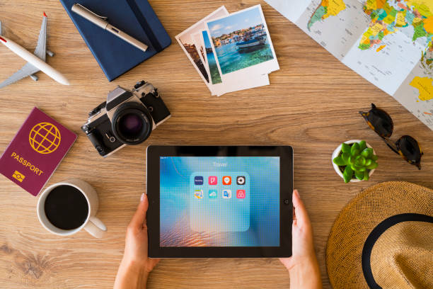 İstanbul, Turkey - August 8, 2018: Woman hands holding a tablet pc on a wooden desk with travel accessories. The tablet pc is an iPad, developed by Apple Inc.